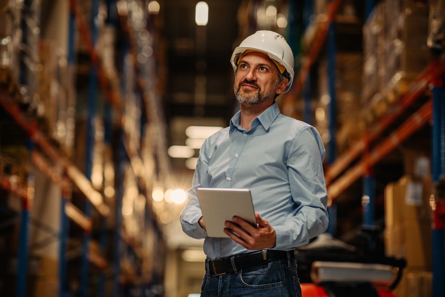 Warehouse worker with a tablet standing in front of a forklift
